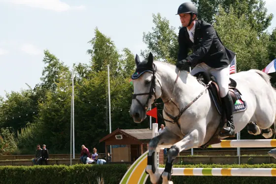 A grey horse jumping at a summer show